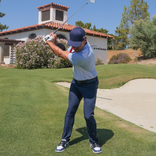 Golfer in action on a golf course with a building and trees in the background