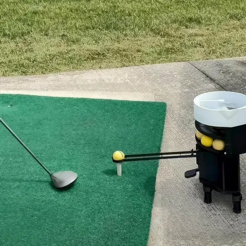 Golf club and balls on a green mat with a golf ball launcher in the background.