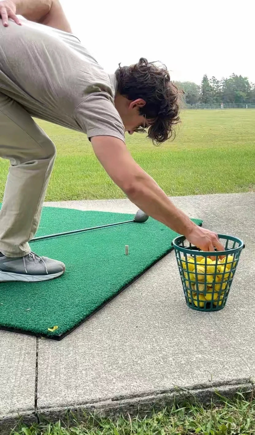 Person practicing golf on a mat with a basket of balls.