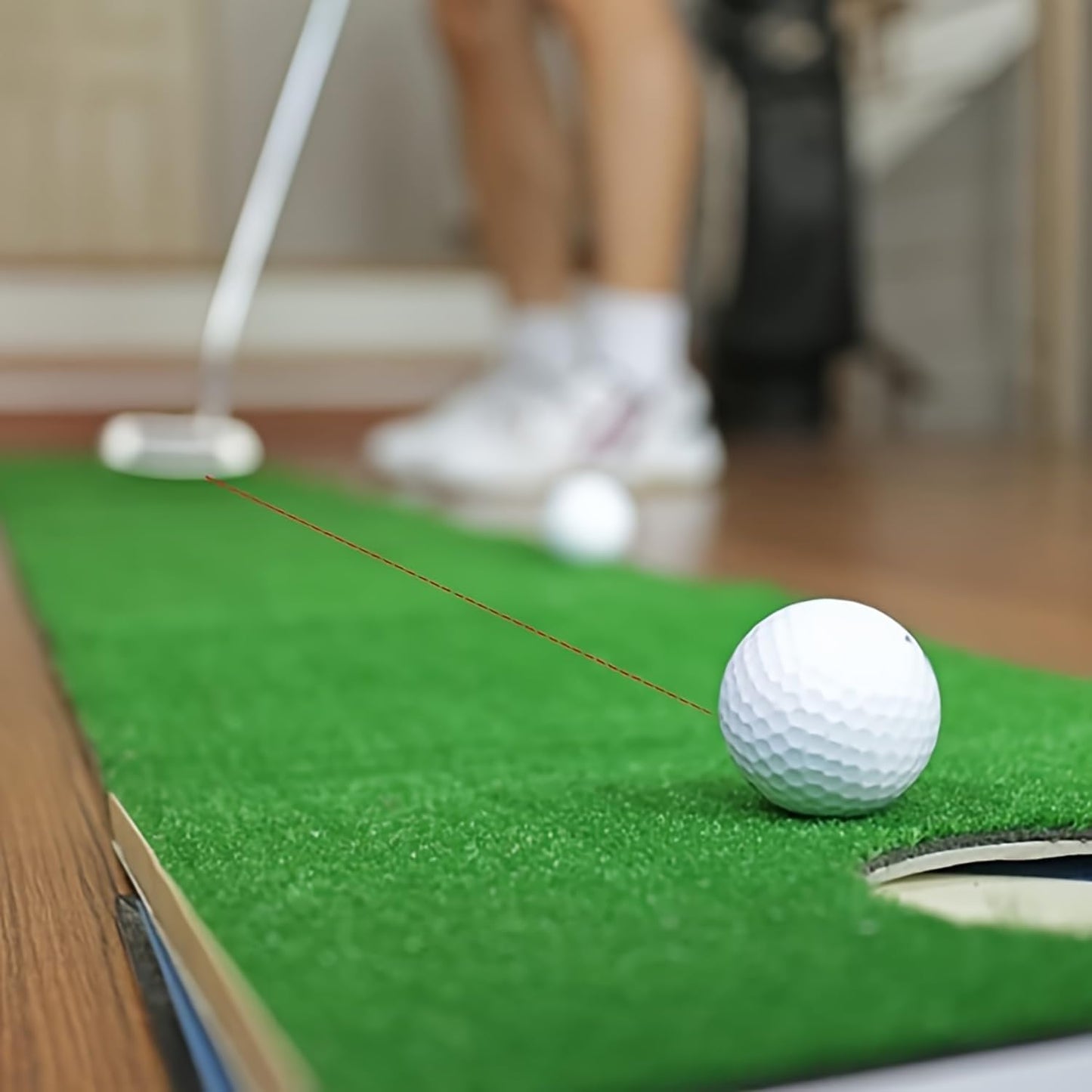 Golf ball on a green mat with a blurred background of a person and golf club.